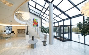 Modern kontorslobby med marmorgolv, en spiraltrappa, stora fönster, abstrakt väggkonst och moderna möbler.
