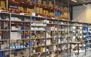 Industriella lagerhyllor fyllda med olika förpackade produkter och föremål organiserade efter rader och sektioner.